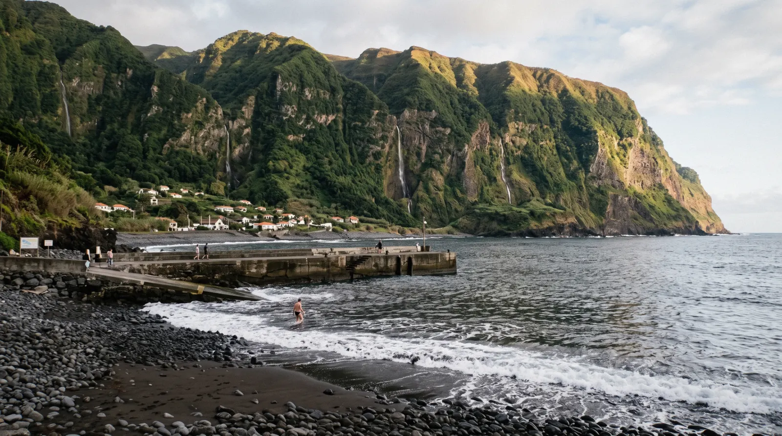 The black pebble beach and pier at Seixal under green cliffs on the north coast, Madeira, Portugal
