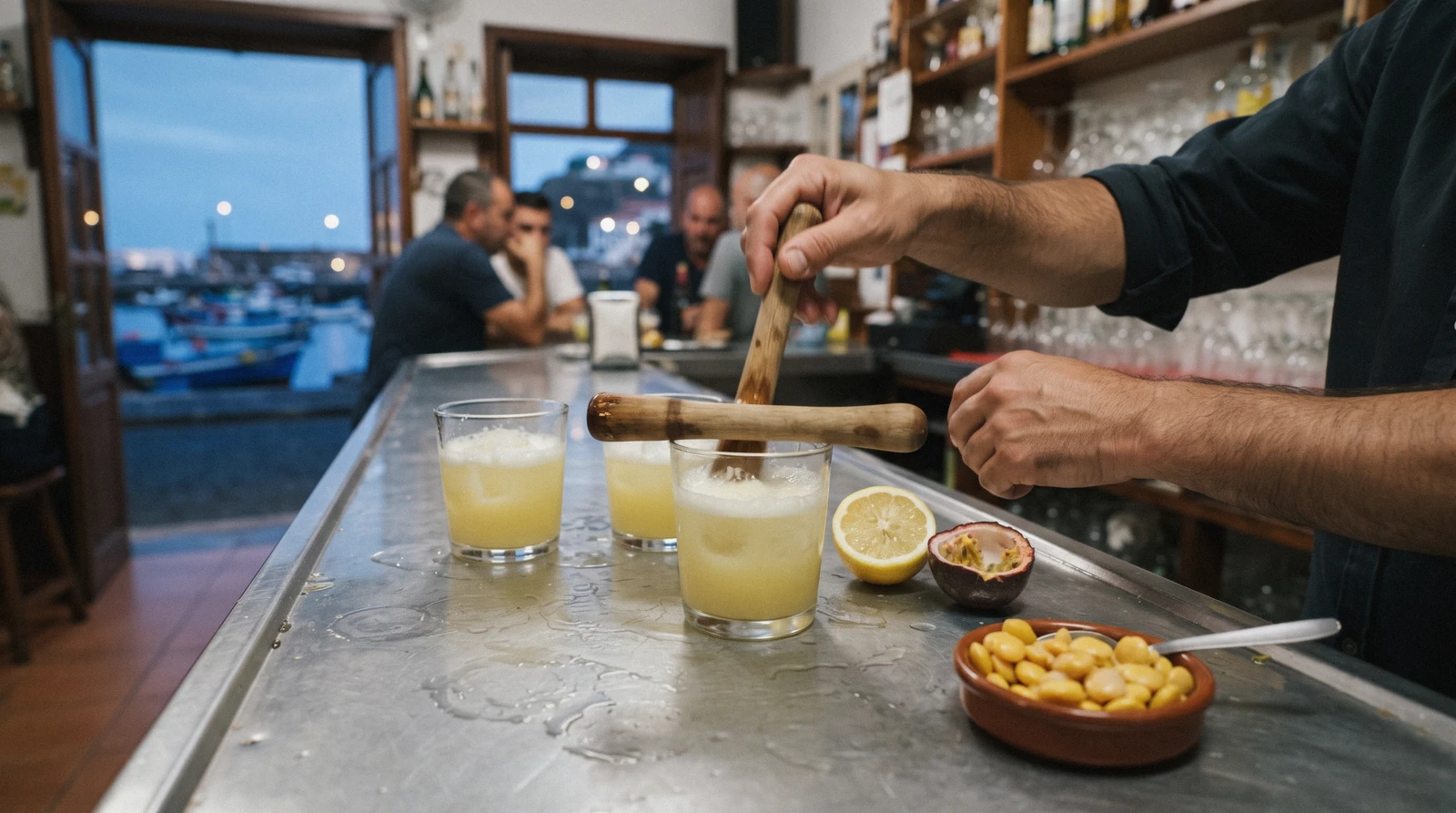 Three glasses of cloudy poncha with a wooden mexelhote and a halved lemon on a bar counter in Câmara de Lobos, Madeira